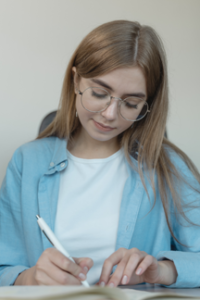 teen in blue and white shirts writes on paper using white pen