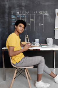 teen in yellow tee and checkered pants holds ipad in classroom