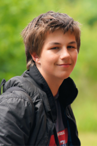 teen in black jacket with backpack smiles at camera