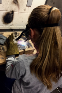 teen with long ponytail and safety glasses welds