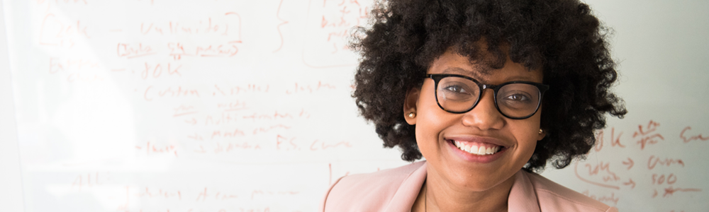 teacher in pink blazer stands in front of whiteboard